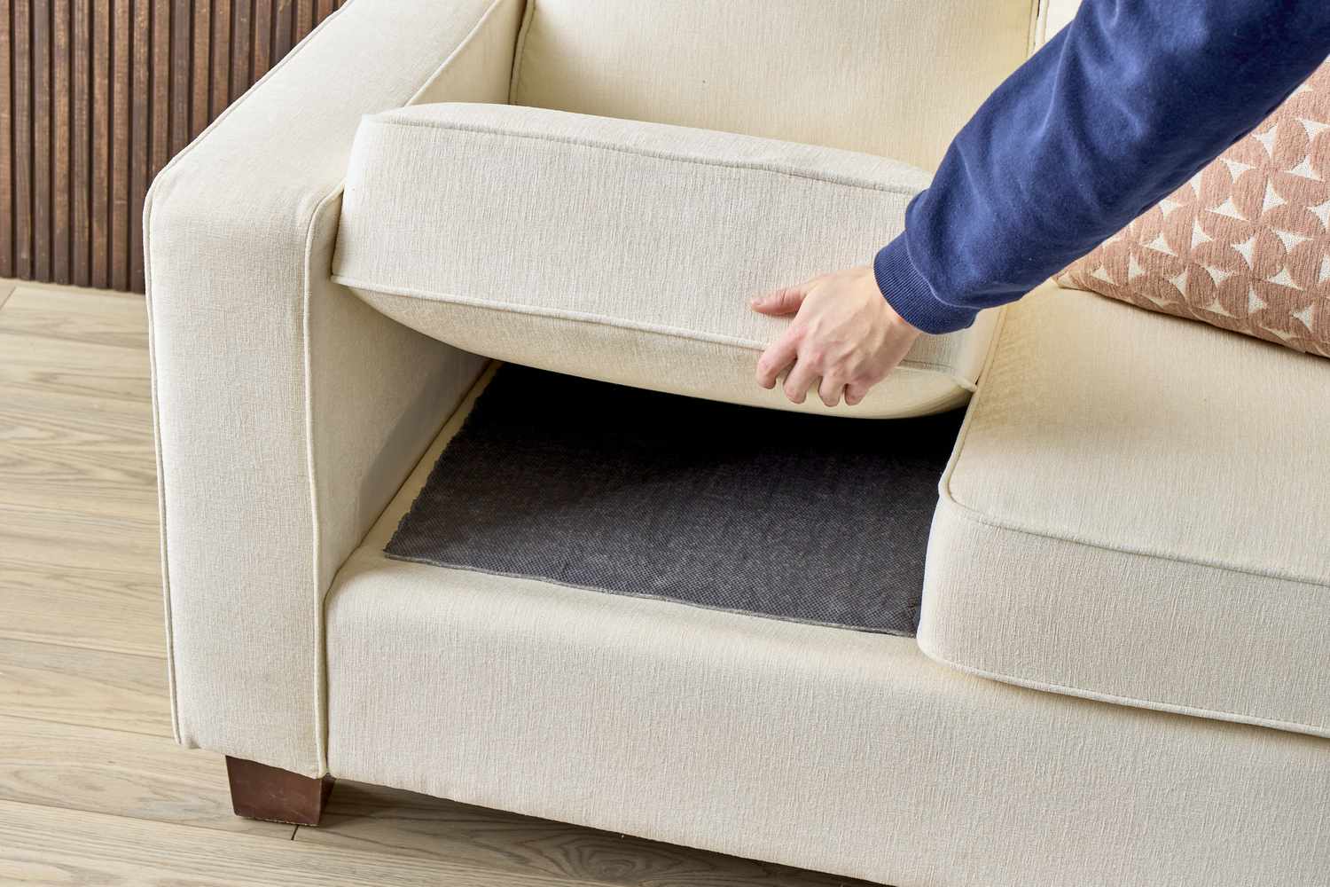 Hands sliding a thin textured nonslip liner between a foam cushion insert and a fabric cushion cover, close-up realistic photo