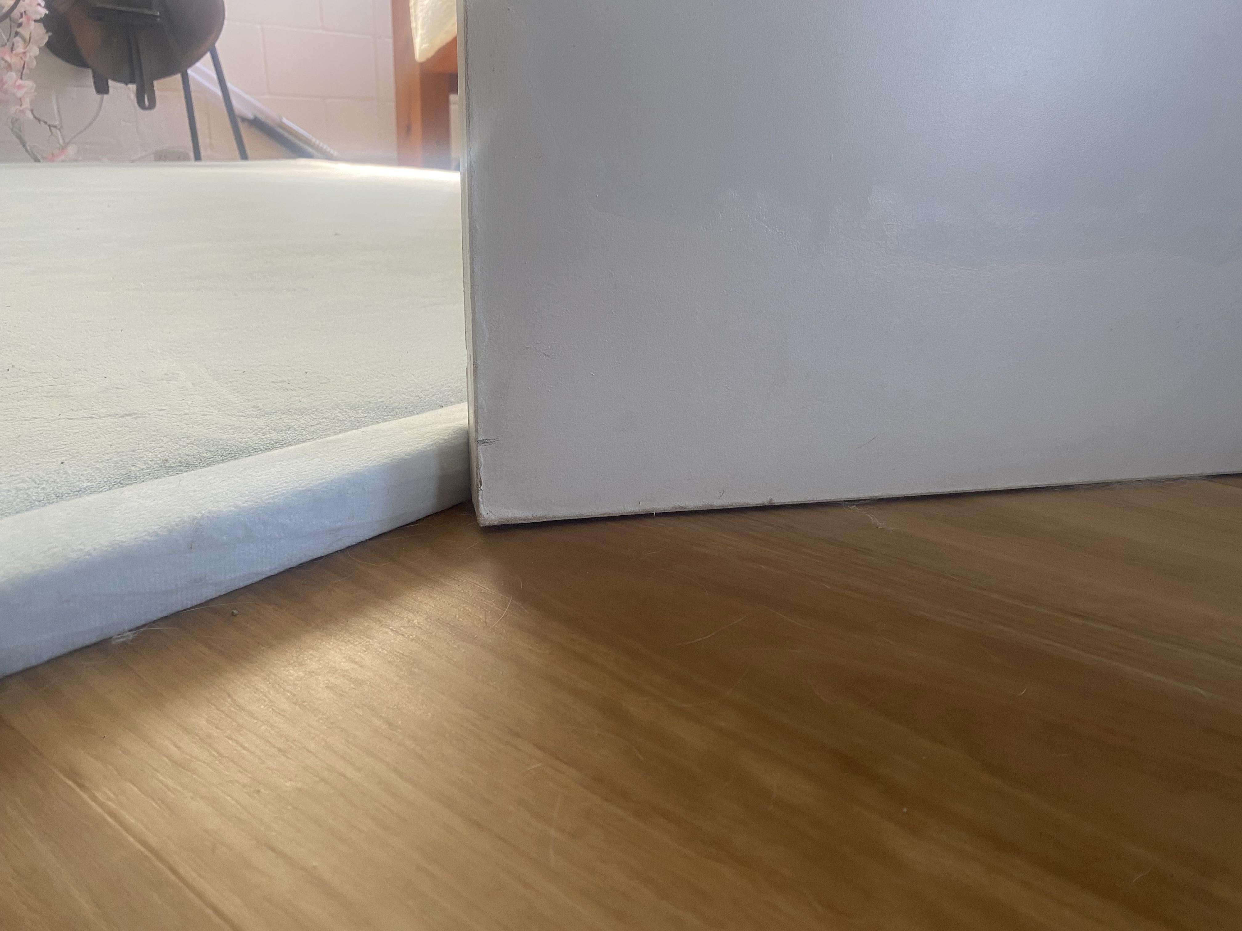 Hands using scissors to trim a rug pad so it stops short of a doorway on a wood floor