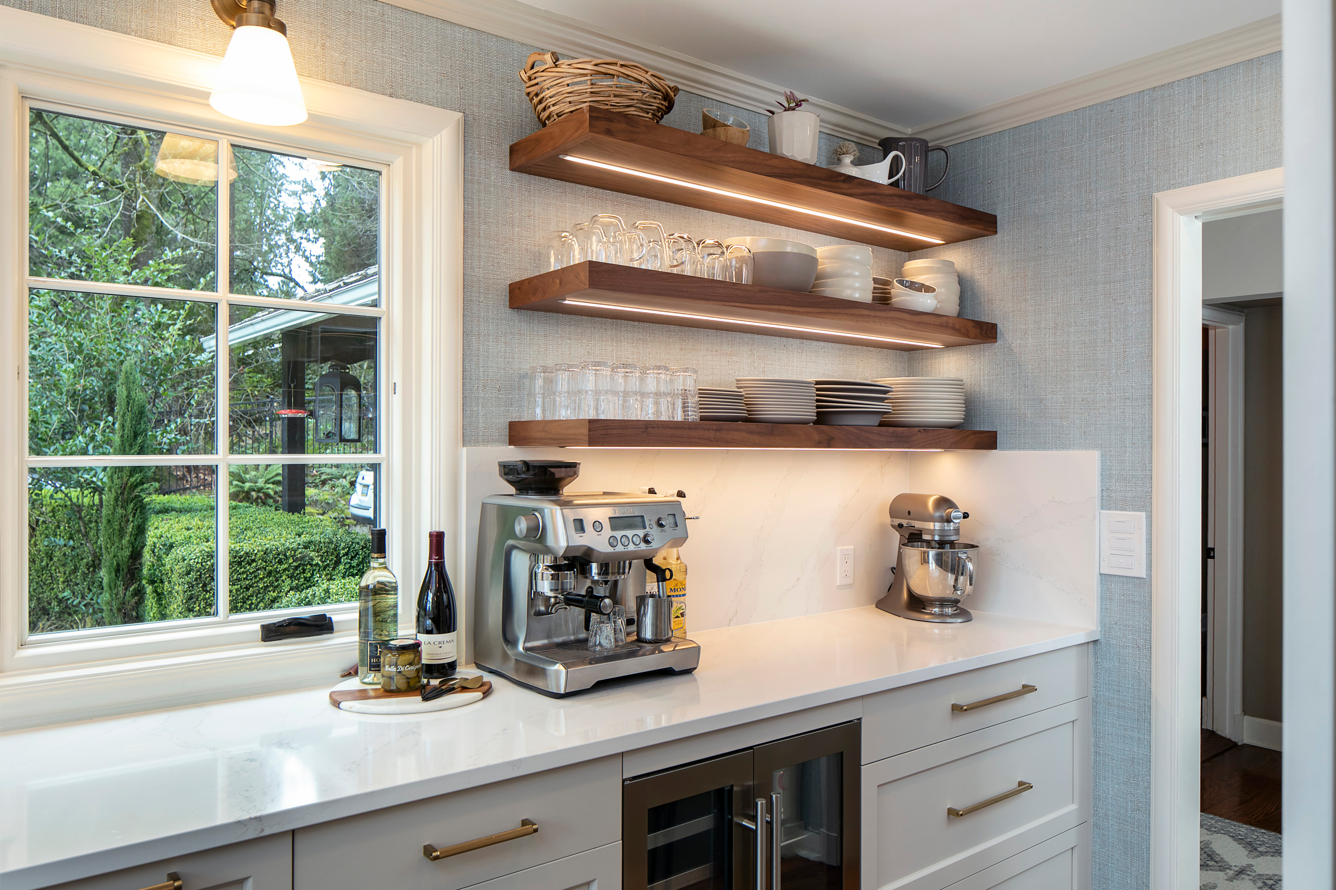 Open kitchen shelves lit by warm under-shelf lights, highlighting glassware and neutral ceramics against a softly colored wall