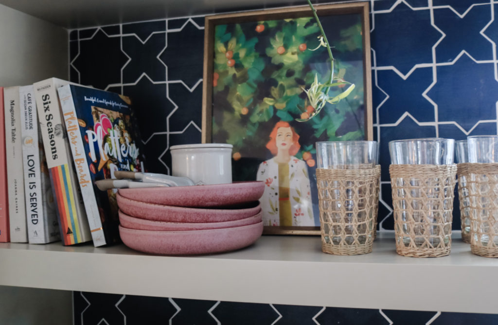 Open kitchen shelves with a stack of white plates, two wooden cutting boards leaned upright, and a small ceramic bowl in warm natural light