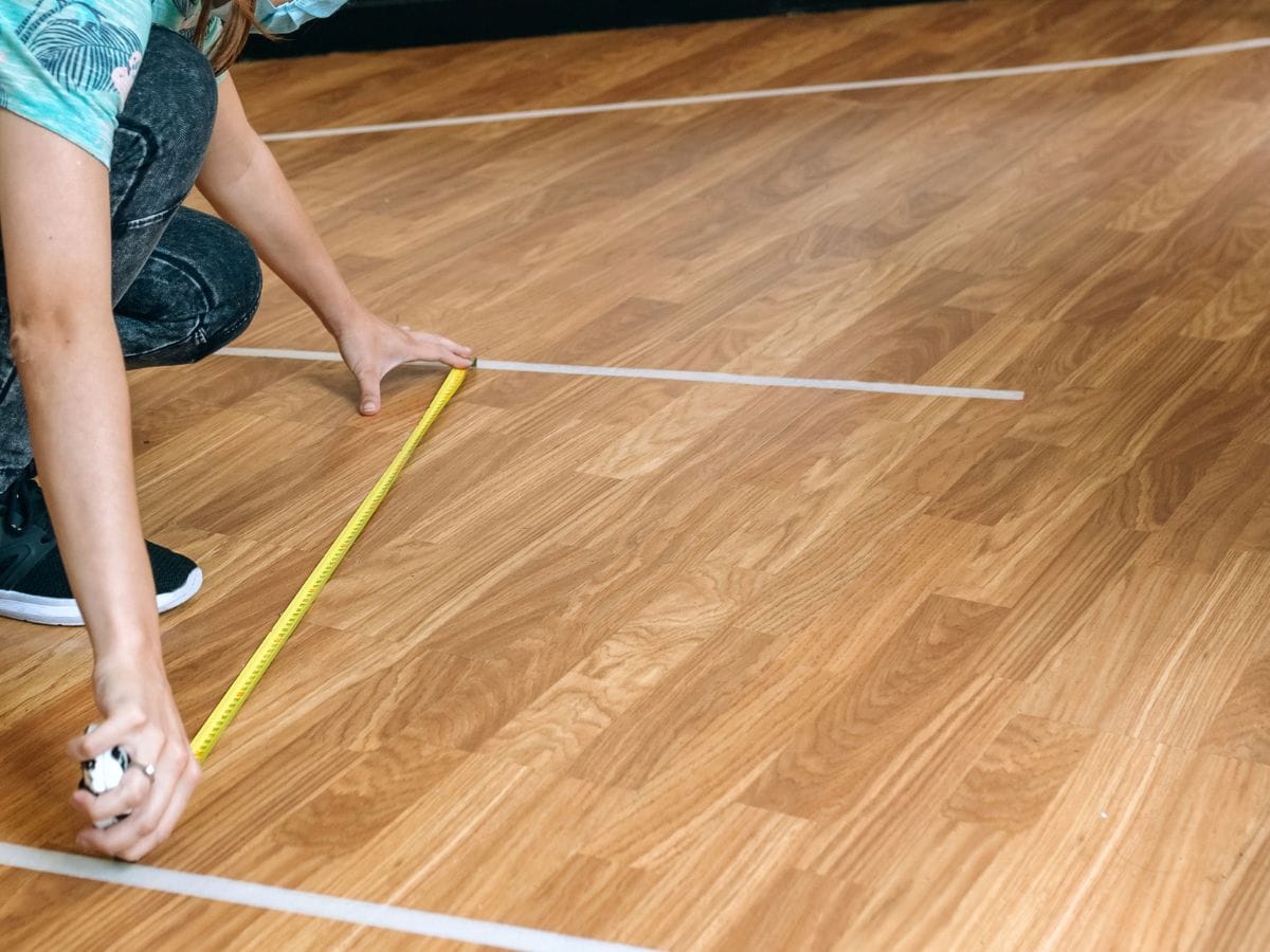 Painter’s tape on an apartment floor marking the outline of a sofa near a hallway corner, realistic home photography