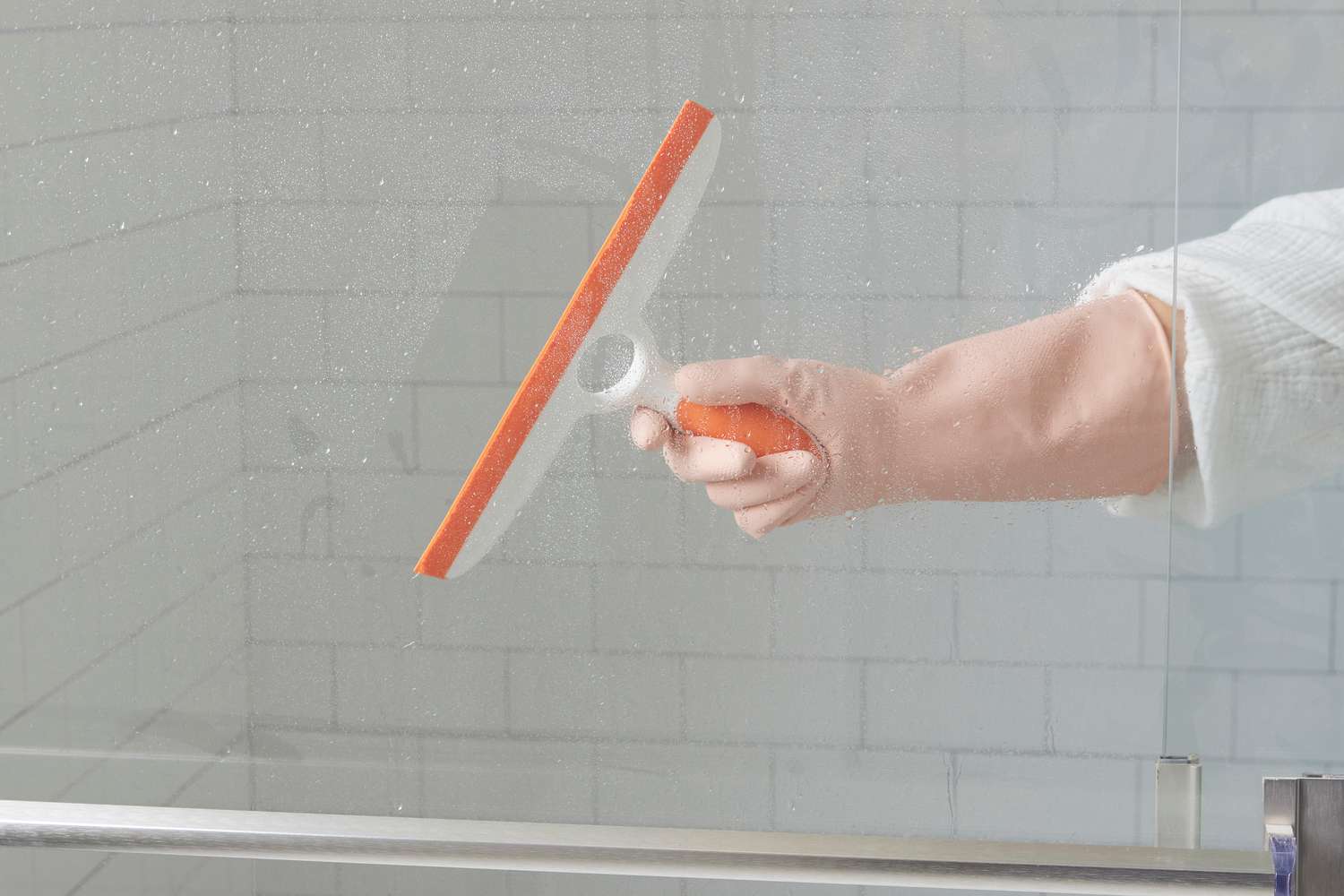 Paper towels pressed onto a glass shower door, visibly damp with vinegar solution to treat hard water spots, real photo