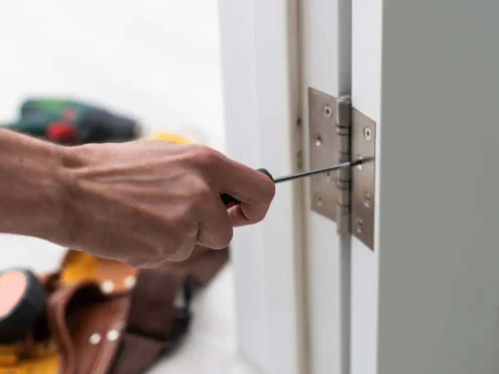 Primer plano de una mano apretando los tornillos de una bisagra en una puerta interior blanca con marco de madera, foto realista en luz natural