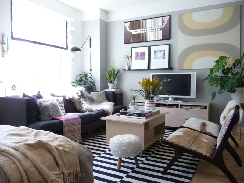 Small apartment living room with a compact sofa, one accent chair, a round coffee table, and a rug under the front legs of the seating