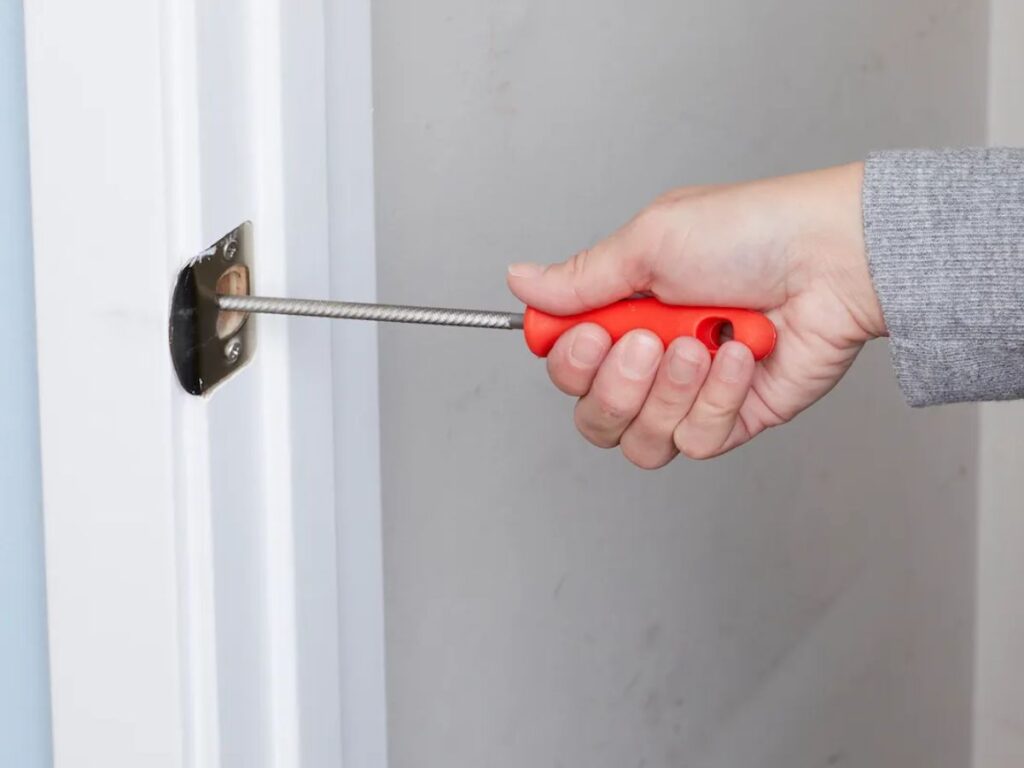 Una persona aflojando los tornillos de la placa del recibidor de una cerradura en el marco de una puerta para alinearla con el pestillo, fotografía realista
