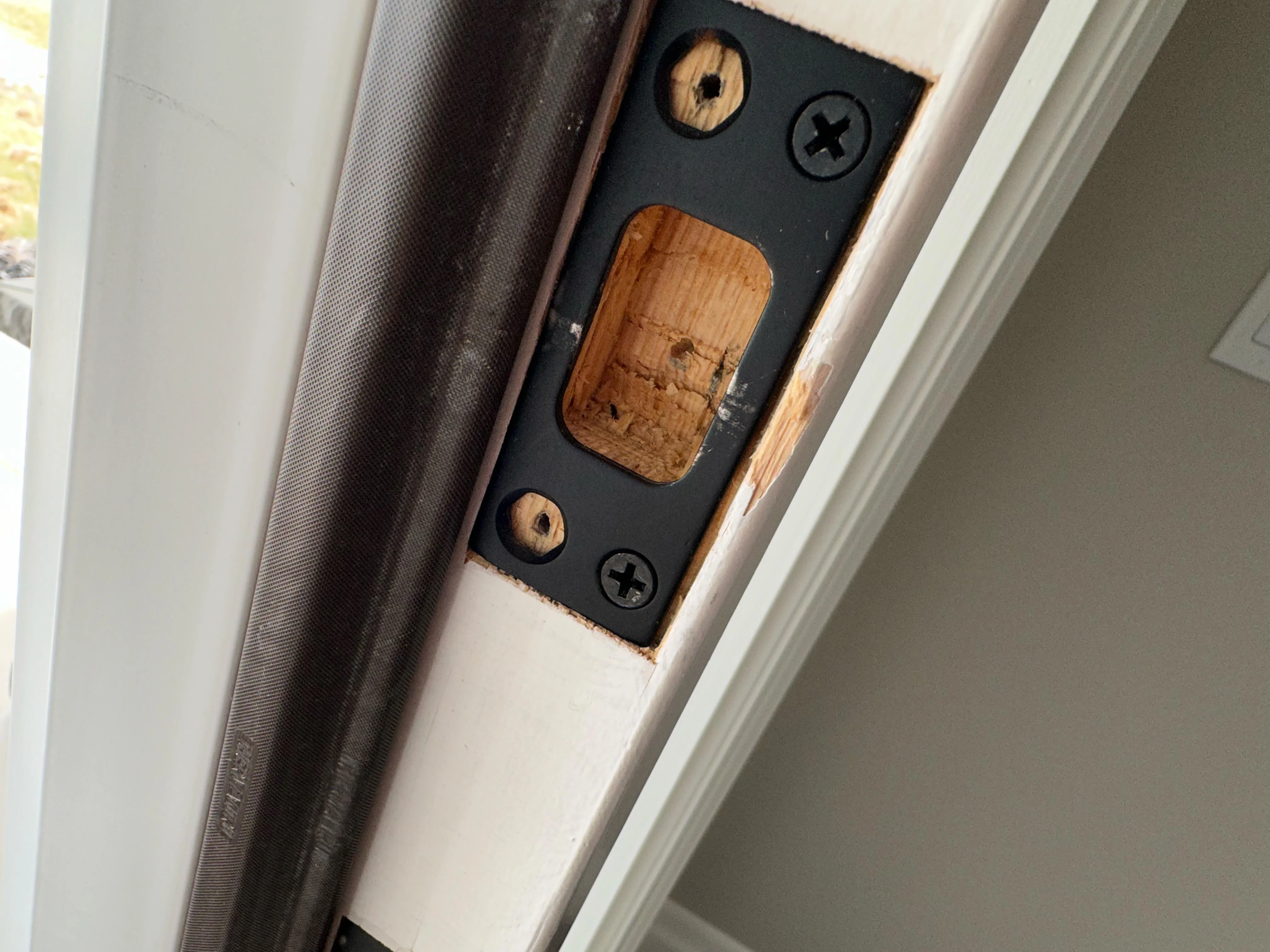 Una placa metálica del pestillo en el marco de una puerta interior, mostrando marcas de roce donde el pestillo golpea antes de entrar, fotografía realista